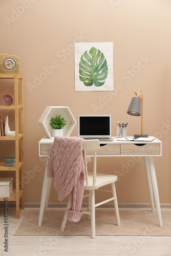 Cozy workplace with modern laptop on desk and comfortable chair at home © New Africa