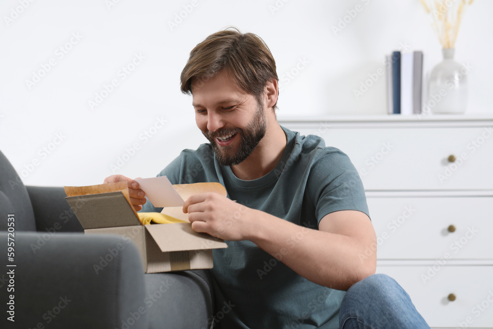 Happy man with greeting card near parcel at home. Internet shopping Happy man with greeting card near parcel at home. Internet shopping