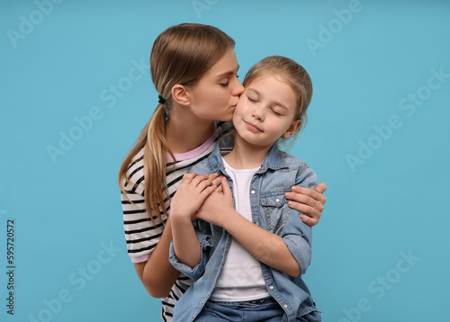 Young woman kissing her little daughter on light blue background. Happy Mother's Day