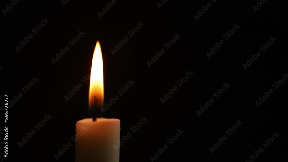 Close-up frame. A single wax white candle is burning. Orange light flame. The wind blows back and forth. black darkness background night Close-up frame. A single wax white candle is burning. Orange light flame. The wind blows back and forth. black darkness background night