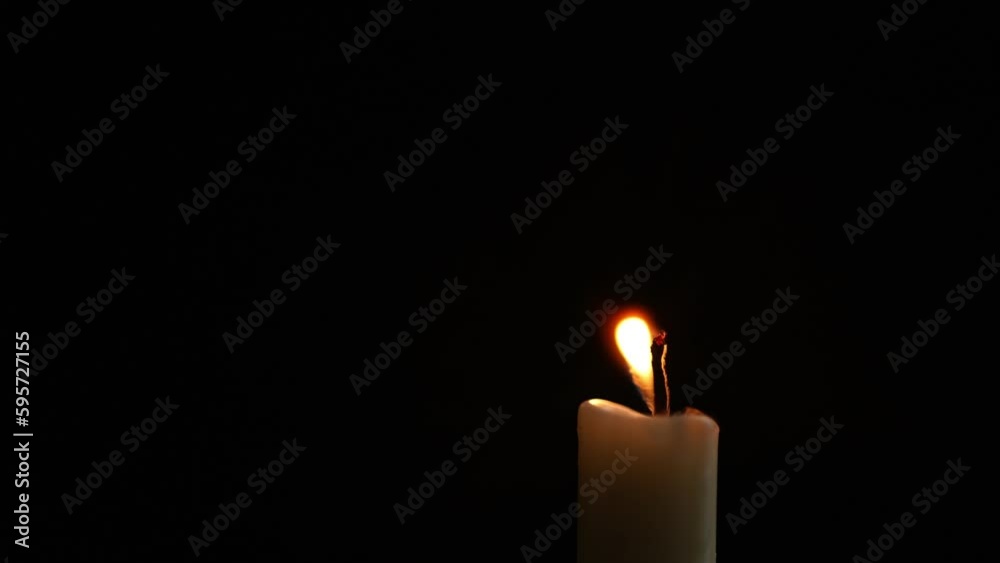 Close-up frame. A single wax white candle is burning. Orange light flame. The wind blows back and forth. black darkness background night Close-up frame. A single wax white candle is burning. Orange light flame. The wind blows back and forth. black darkness background night