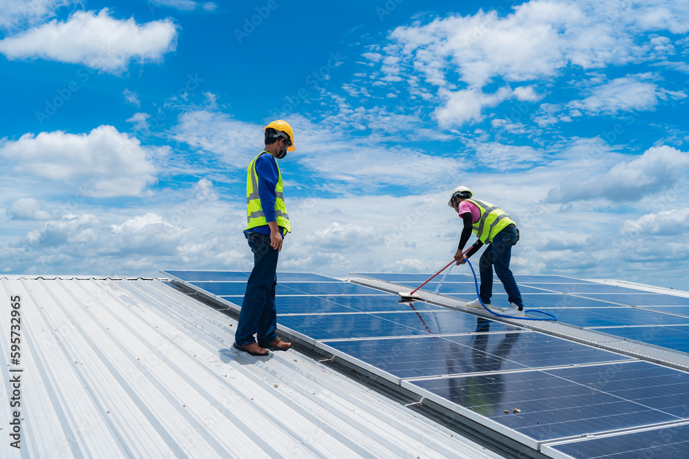 Professional worker cleaning solar panels with brush and washing with water on roof structure of building factory. Technician using mop to clean the dirty and dust, green electricity energy technology Professional worker cleaning solar panels with brush and washing with water on roof structure of building factory. Technician using mop to clean the dirty and dust, green electricity energy technology
