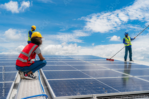 Professional worker cleaning solar panels with brush and washing with water on roof structure of building factory. Technician using mop to clean the dirty and dust, green electricity energy technology