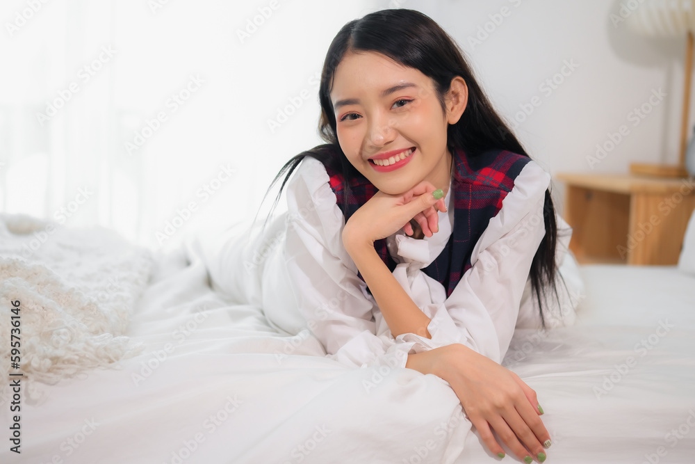 Beautiful asian girl lying on a white bed in bedroom and looking to the camera with a smile on her face. Beautiful asian girl lying on a white bed in bedroom and looking to the camera with a smile on her face.