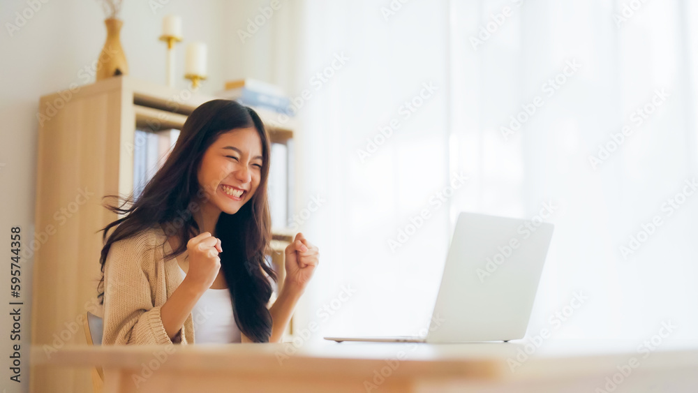 Funny euphoric young asian woman celebrating winning or getting ecommerce shopping offer on computer laptop. Excited happy girl winner looking at notebook celebrating success - obrazy, fototapety, plakaty 
