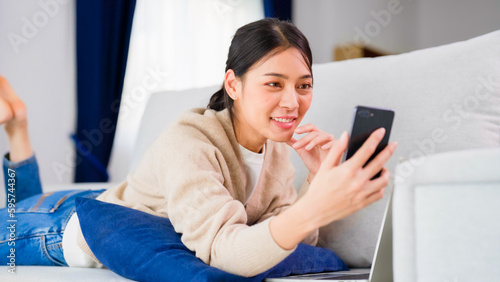 Young asian woman using smart phone at home. Smiling female making video call meeting smartphone at house  messaging or browsing social networks while relaxing on couch