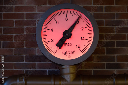 Close-up of a pressure gauge showing the high pressure in the pipe, against the background of a brick wall. Close-up pressure monitoring sensor