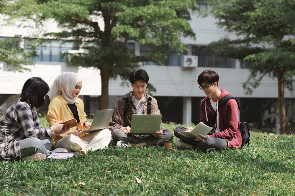 A multiethnic group of asian university students is seen studying together while sitting on the grass near the campus.