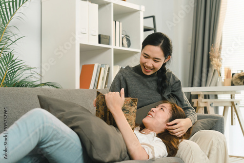 A young Asian LGBT lesbian couple is sharing moments of love and happiness while lying down on the sofa in the living room at home.