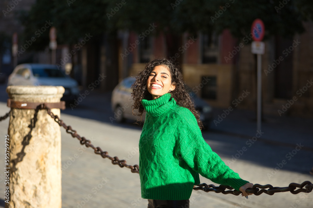 Young, beautiful, brunette woman with curly hair and a green turtleneck  sweater, leaning on a big chain smiling and happy. Concept beauty, fashion,  autumn, winter, cold, happiness. Stock Photo | Adobe Stock