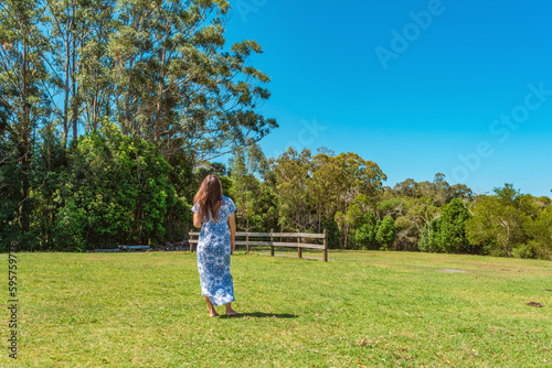 Middle age woman bare feet long brown hair wearing long blue dress back view   walking on green field in bush  Pomona country side Sunshine Coast Australia