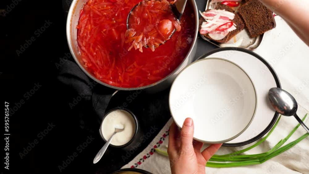 Woman holding clay bowl with Ukrainian borsch. Traditional Ukrainian Russian borscht with white beans on the bowl. Plate of red beet root soup borsch on black rustik table. Beetroot soup Top view