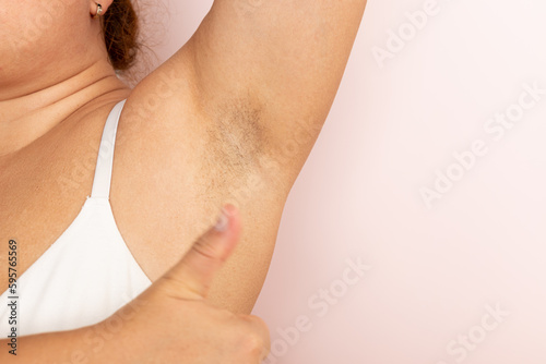 Woman with hairy underarms closeup  free copy space  beige background. Raised arm with armpit hair. Female beauty trend  freedom  skin care  feminism  body positive  naturalness. Hygiene concept.