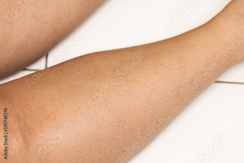 Closeup unshaven hairy woman outstretched legs on white tile. Body positive and feminism for diverse people. Sensitive female skin care and body care. No more epilations. Hormone health problems © Юля Бурмистрова