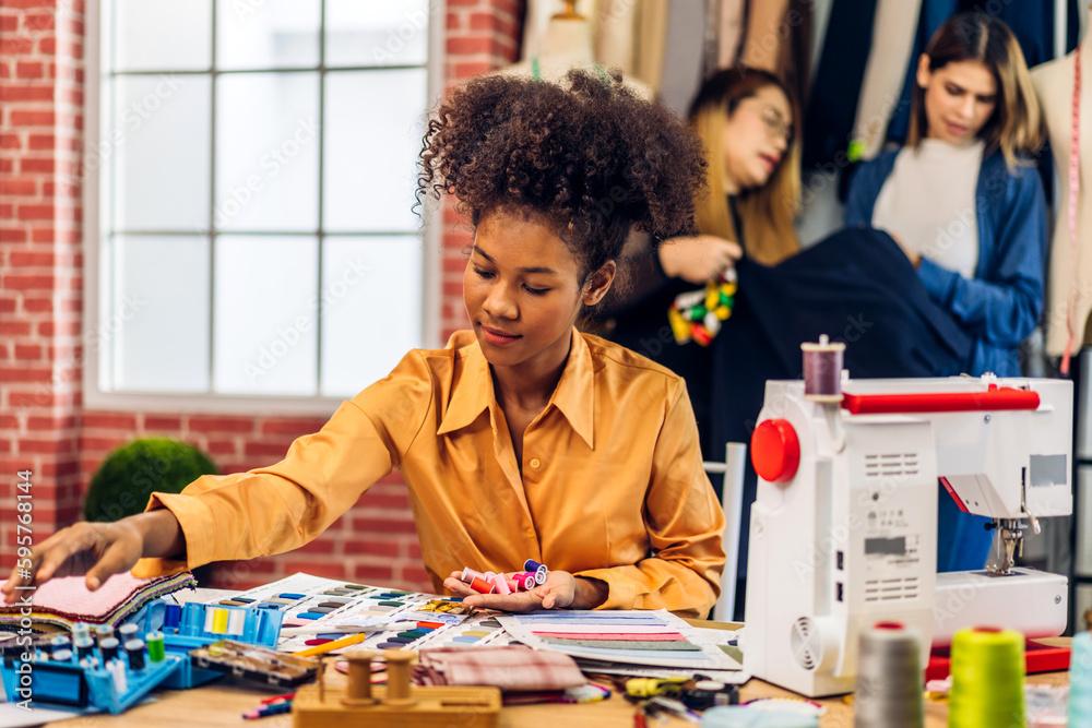 Fototapeta premium Portrait of young african american woman fashion designer stylish sitting and working with color samples.Attractive young african girl work with colorful fabrics at fashion studio