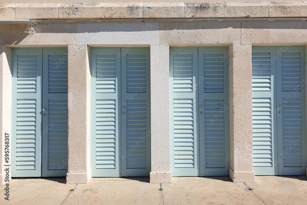 blue shutter doors in a row against cement rendered wall located outdoos on a sunny day at beach