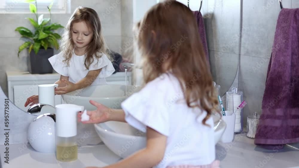 Girl in the washroom. A little girl 4-5 years old washes her hands by herself, standing in front of a large mirror in slow motion. Children's hygiene Girl in the washroom. A little girl 4-5 years old washes her hands by herself, standing in front of a large mirror in slow motion. Children's hygiene