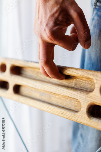 strong male hand of a rock climber holds a board for training finger strength. climbing workout at home. rock climber's hand close-up. strength and endurance. fingerboard and hangboard