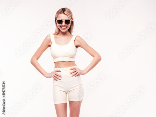 Young beautiful smiling blond female in summer cycling shorts clothes. Sexy carefree woman posing on white background in studio. Positive model having fun indoors. Cheerful and happy. In sunglasses