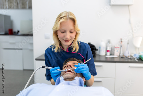 Dentist in blue uniform doing teeth procedure to patient, male patient during treatment procedure in contemporary dental clinic