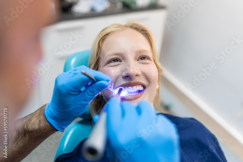 Patient in the dental clinic. Teeth whitening UV lamp with photopolymer composition. Young woman during teeth whitening procedure with curing UV light at dentist s office.