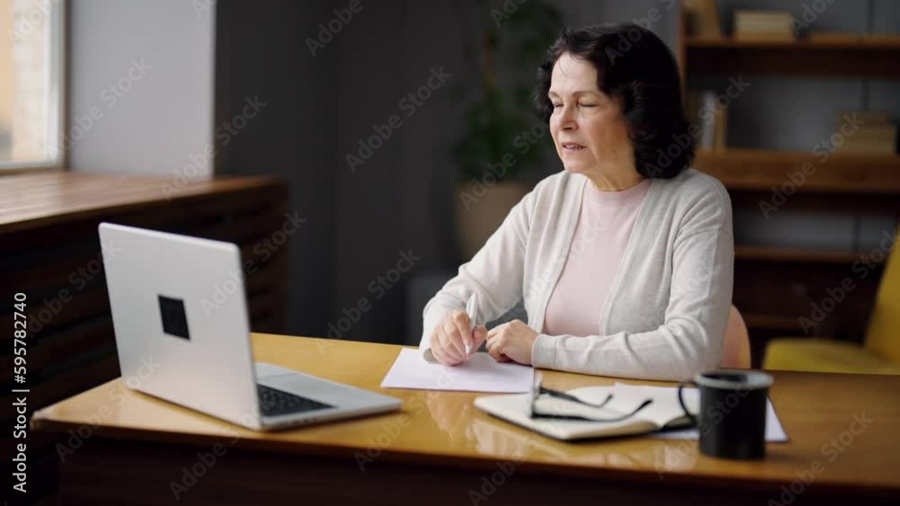 Smiling positive senior woman ending work on laptop, stretching arms sitting at table on workplace in office. Elderly specialist, professional female does job on computer. Old office worker concept.