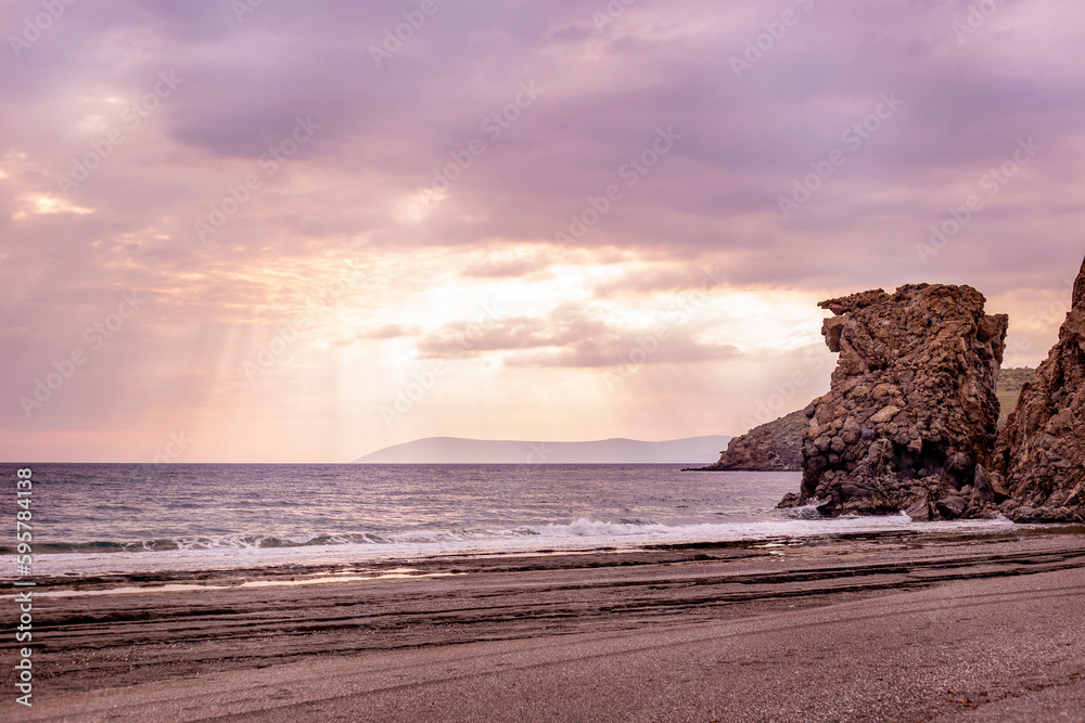sea and huge rocks mountains at cloudy sunset with sun rays purple tones selective focus, natural background with copy space for text