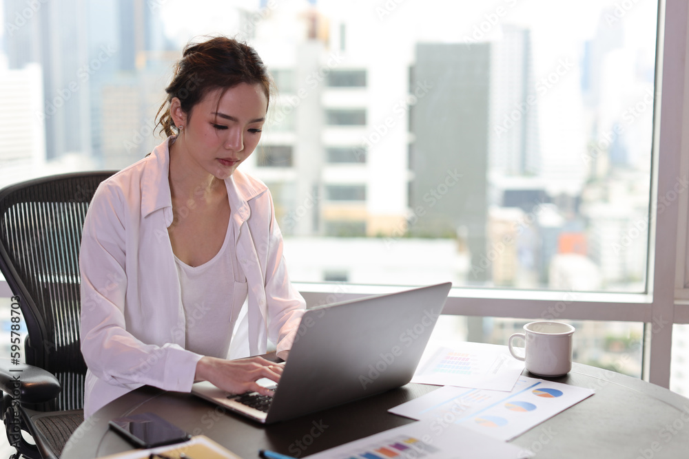 Portrait of confident and beautiful young asian businesswoman with happy emotion sitting and using computer in modern hotel with city blurred background. Success business and lifestyle concept