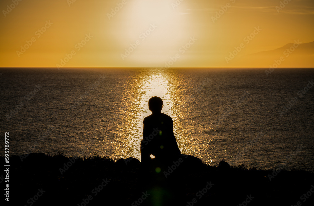 Silhouette of man sitting on rock looking at sea view during sunset