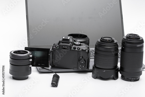 Aparat fotograficzny cyfrowy i obiektywy oraz akcesoria obok laptopa na białym tle
