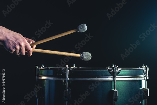 A man plays a musical percussion instrument with sticks on a dark background.