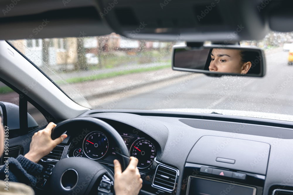 Woman drive a car reflects in back view mirror.