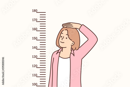 Teenage girl measures height standing near marks on wall, wanting to become tall
