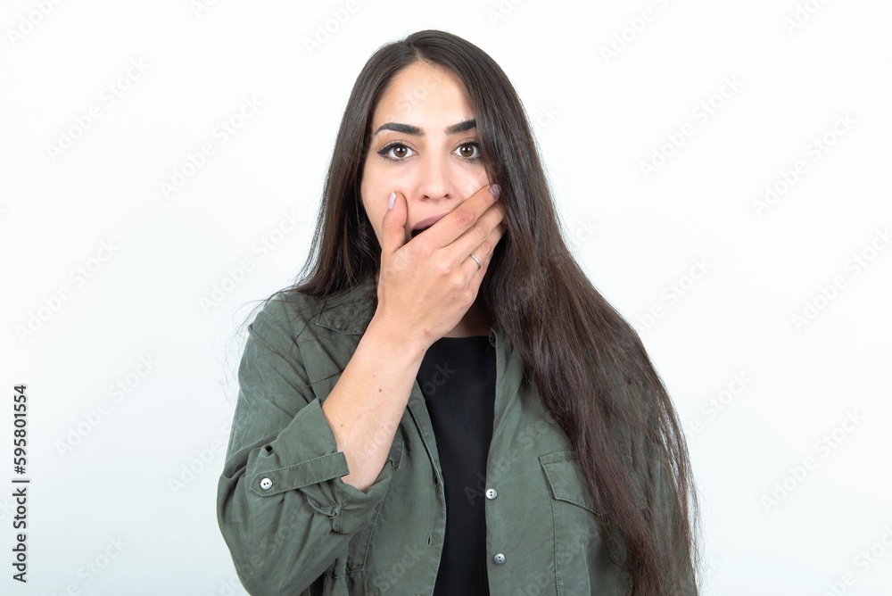 Emotional young brunette woman wearing casual clothes over white studio background gasps from astonishment, covers opened mouth with palm, looks shocked at camera. Emotional young brunette woman wearing casual clothes over white studio background gasps from astonishment, covers opened mouth with palm, looks shocked at camera.