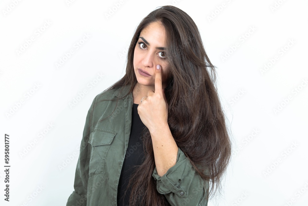 young brunette woman wearing casual clothes over white studio background Pointing to the eye watching you gesture, suspicious expression. young brunette woman wearing casual clothes over white studio background Pointing to the eye watching you gesture, suspicious expression.