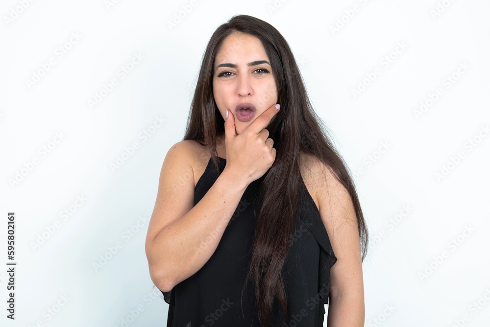young brunette woman wearing black blouse over white studio background Looking fascinated with disbelief, surprise and amazed expression with hands on chin young brunette woman wearing black blouse over white studio background Looking fascinated with disbelief, surprise and amazed expression with hands on chin