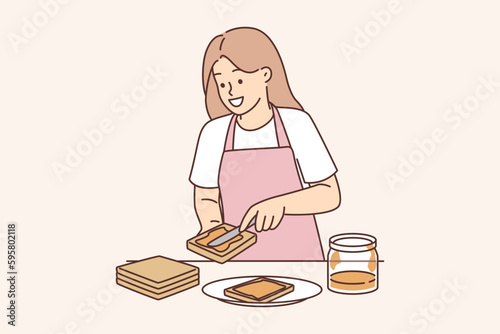 Woman spreads peanut butter on bread preparing sweet breakfast sandwich and smiles
