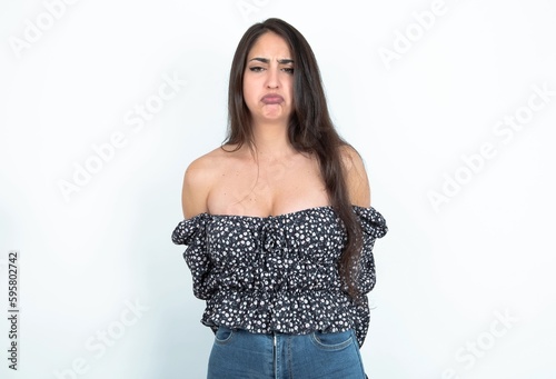 Dismal gloomy rejected young brunette woman wearing a blouse over white studio background has problems and difficulties, curves lower lip and closes eyes in despair, being in depression