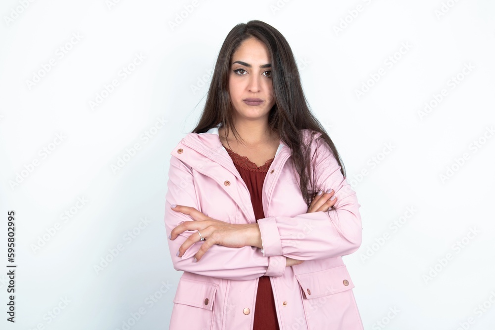 Self confident serious calm young brunette woman wearing pink raincoat over white studio background stands with arms folded. Shows professional vibe stands in assertive pose. Self confident serious calm young brunette woman wearing pink raincoat over white studio background stands with arms folded. Shows professional vibe stands in assertive pose.