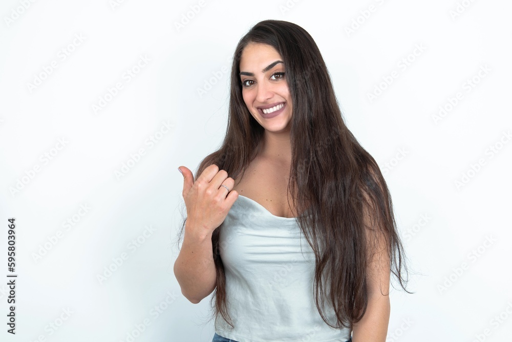 young brunette woman wearing white tank top over white studio background points away and gives advice demonstrates advertisement young brunette woman wearing white tank top over white studio background points away and gives advice demonstrates advertisement