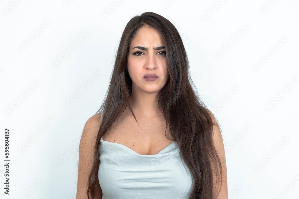 young brunette woman wearing white tank top over white studio background Pointing down with fingers showing advertisement, surprised face and open mouth young brunette woman wearing white tank top over white studio background Pointing down with fingers showing advertisement, surprised face and open mouth