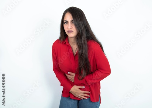 Young brunette woman wearing red shirt over white studio background got stomachache