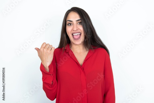 Impressed Young brunette woman wearing red shirt over white studio background point back empty space