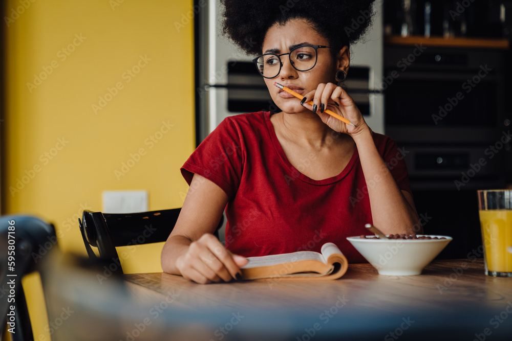 African woman studying while having breakfast in kitchen