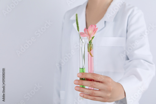 Woman holds test tubes with flower against light background