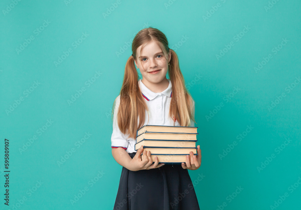Smiling little blonde girl 10-12 years old in school uniform with backpack holding books isolated on pastel blue background studio portrait. The concept of children's lifestyle. Education at school. Smiling little blonde girl 10-12 years old in school uniform with backpack holding books isolated on pastel blue background studio portrait. The concept of children's lifestyle. Education at school.