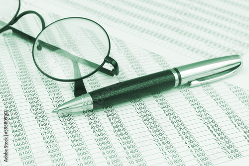 Round eyeglasses and metallic pen on financial reports papers. 