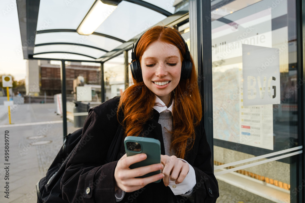 Fototapeta premium Smiling woman using mobile phone while standing at bus station