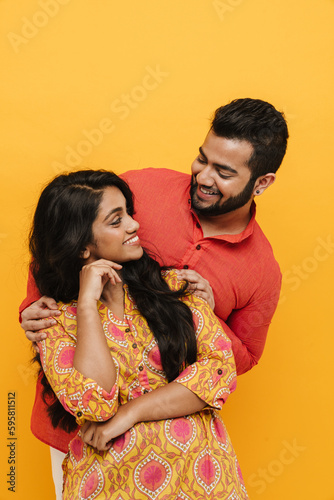 Indian man and woman looking at each other while posing isolated over yellow background