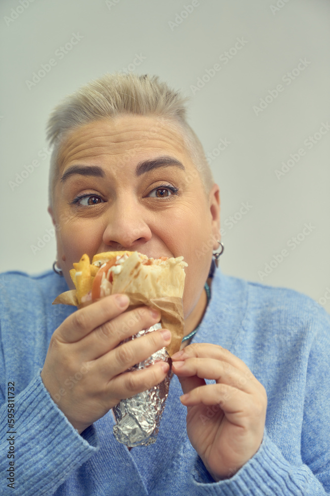 Funny adult woman chewing a sandwich. White female person with short hair eating fast food Funny adult woman chewing a sandwich. White female person with short hair eating fast food